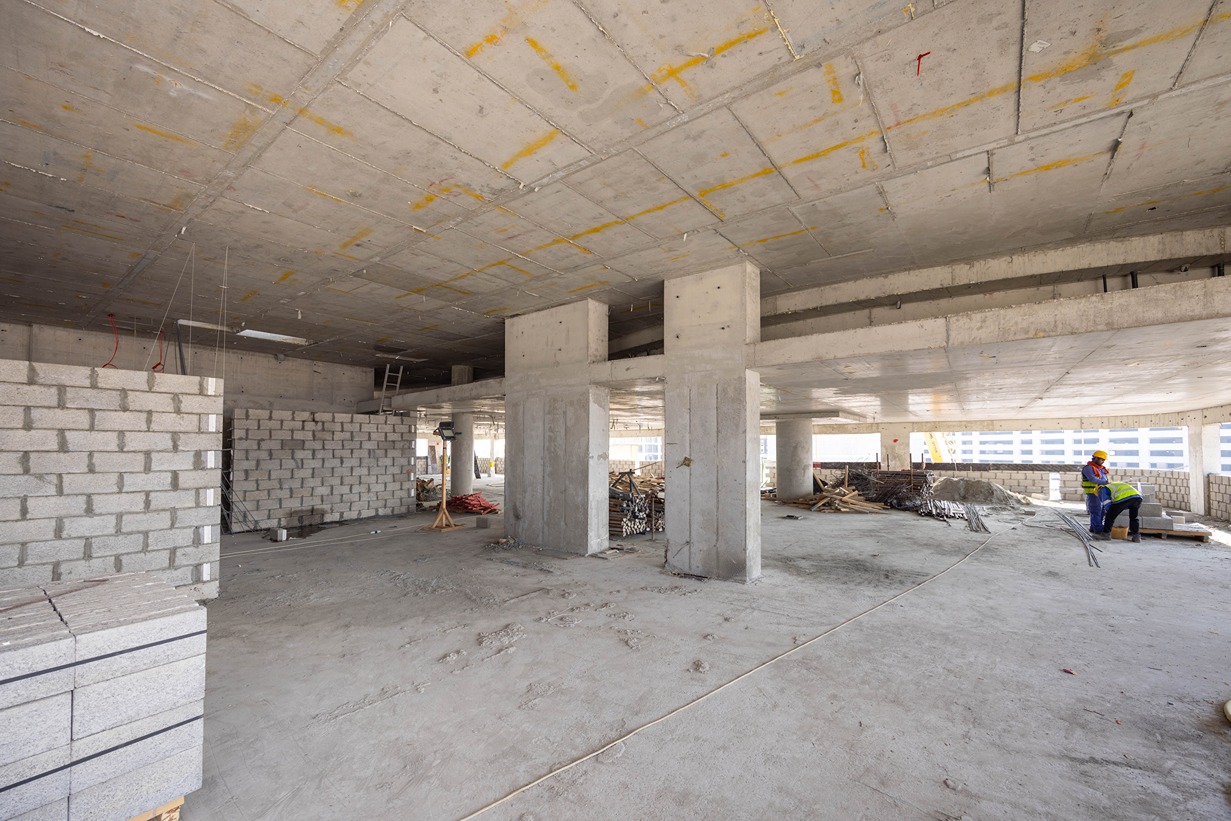 Beach Walk Residence A construction site interior featuring concrete columns, unfinished walls, and workers in hard hats.