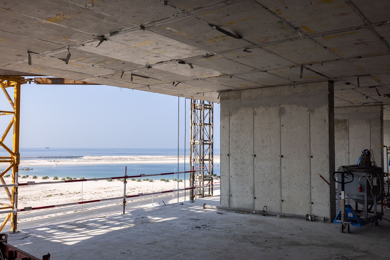 Beach Walk Residence View from an unfinished building showing concrete walls, scaffolding, and a scenic beach with water in the distance.