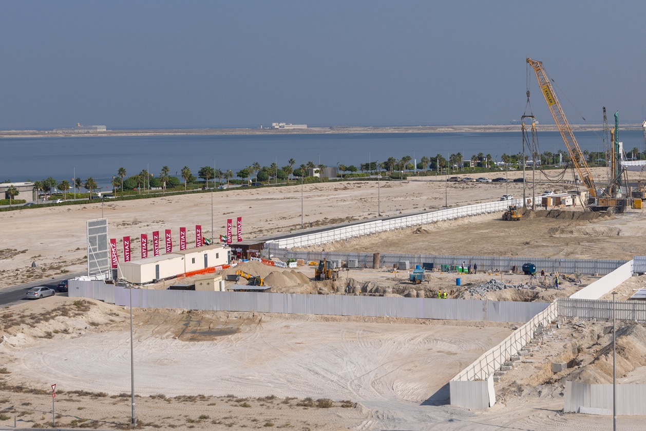 Beach Walk Residence Construction site by the water featuring heavy machinery, sand piles, and workers in a clearing area with flags.