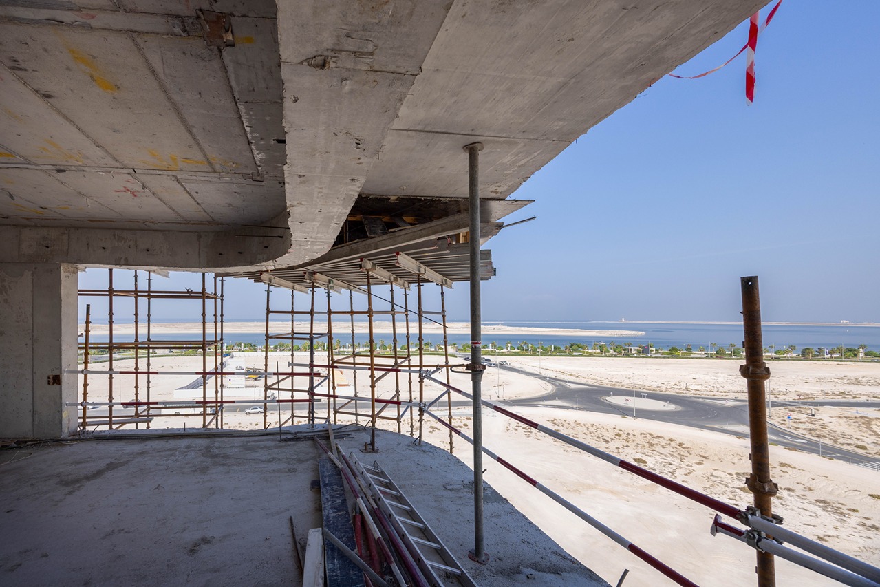 Beach Walk Residence View from a construction site featuring scaffolding, concrete structures, and a distant waterfront landscape.