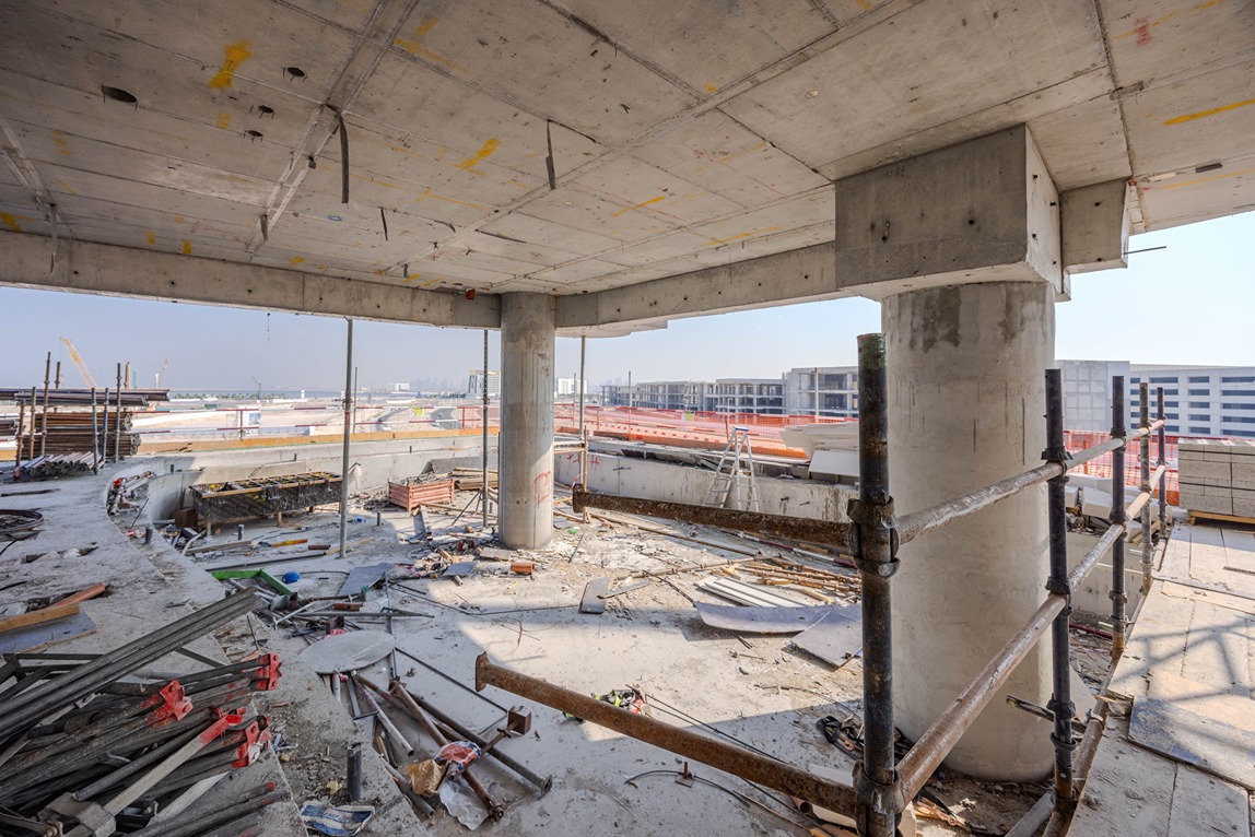 Beach Walk Residence An unfinished building interior showing concrete pillars, construction debris, scaffolding, and a view of the outdoors.