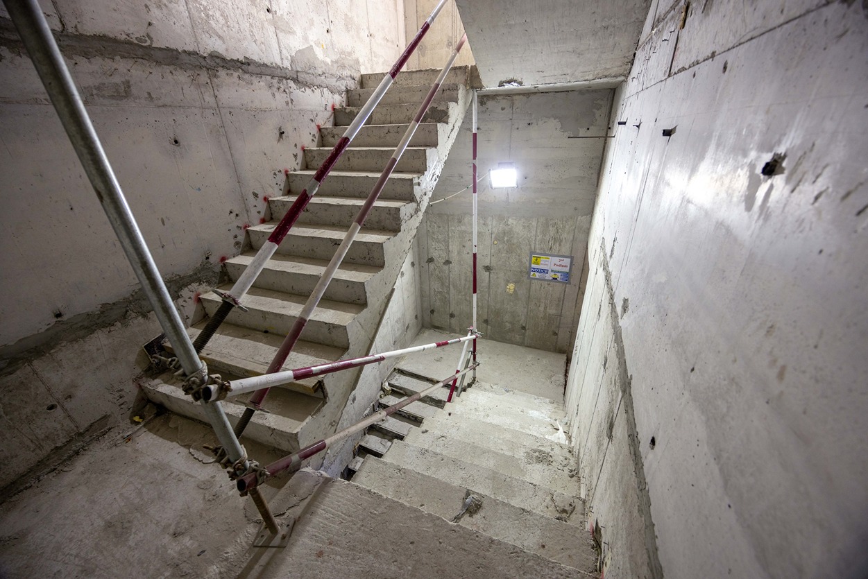 Beach Walk Residence A view of a construction site stairway with concrete steps, scaffolding, and a light source above.