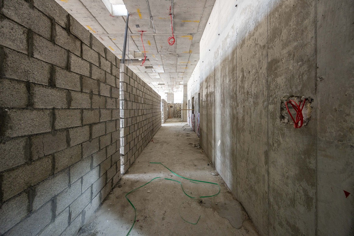 Beach Walk Residence A long, unfinished corridor with gray block walls, concrete surfaces, and scattered construction materials and wires.