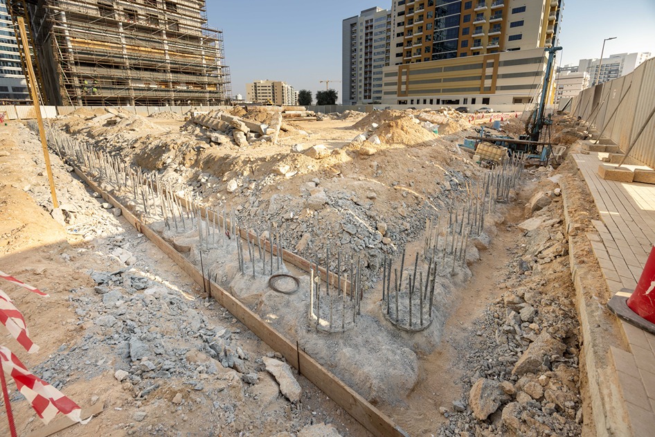 Cove Edition I By Imtiaz 1 Construction site featuring a filled trench with exposed rebar, surrounded by piles of dirt and building materials.