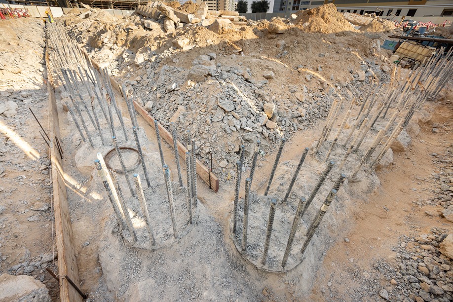 Cove Edition I By Imtiaz 1 Construction site showing excavated ground with rebar columns and piles surrounded by dirt and debris.