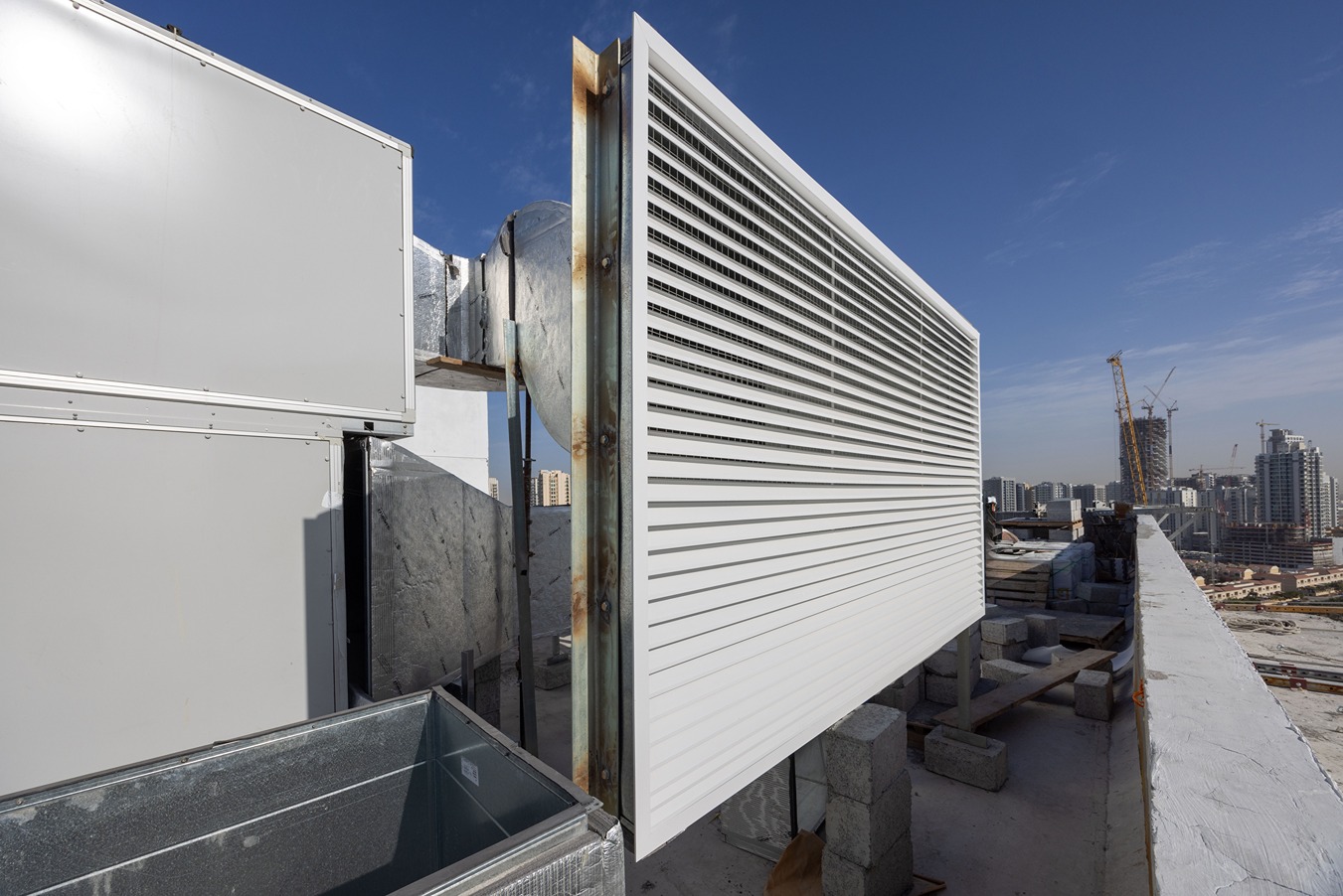 Pearl House By Imtiaz A rooftop installation features a large white air vent, metal ducts, and a construction site in the background.