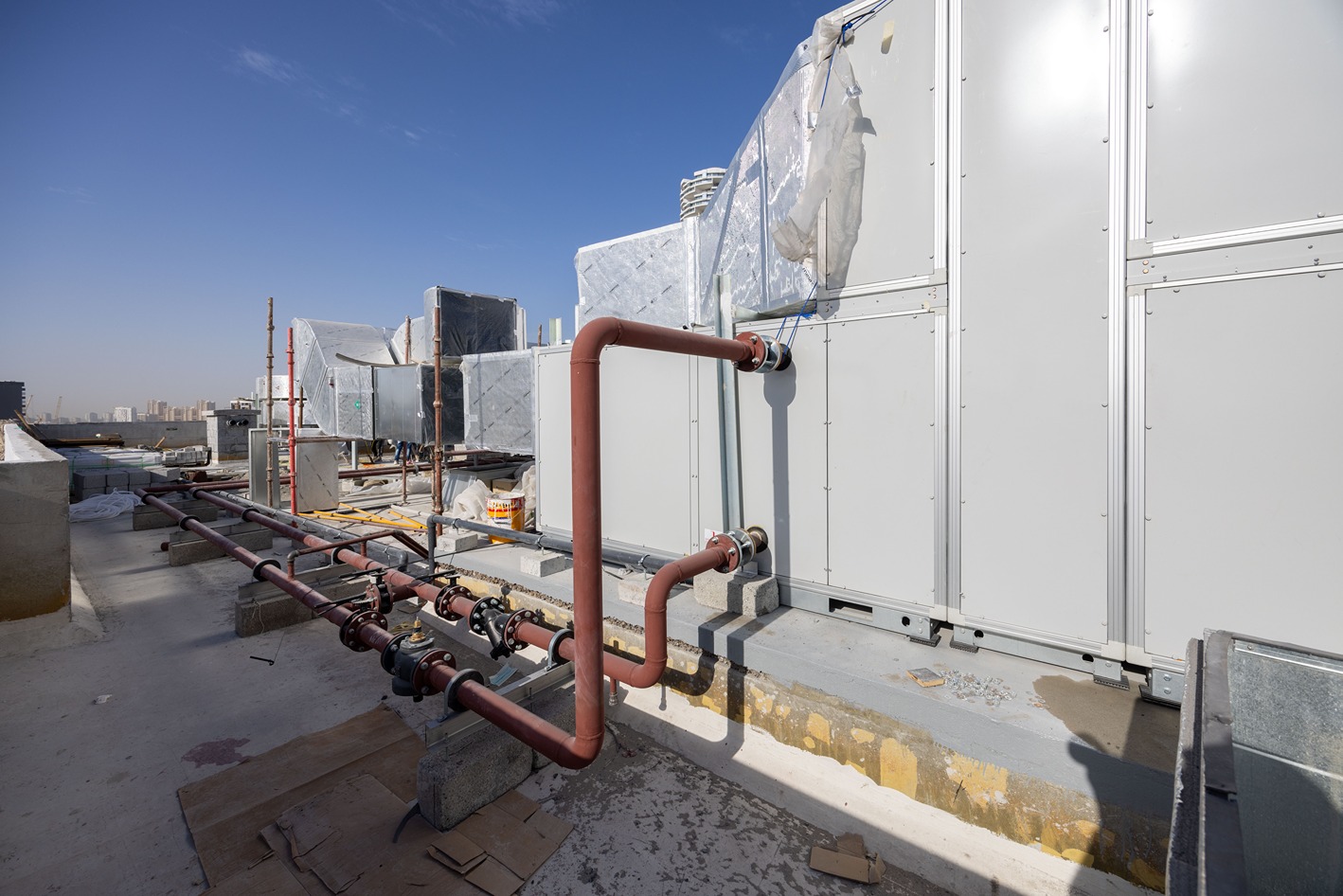 Pearl House By Imtiaz A rooftop scene showing large HVAC units, connecting pipes, and clear blue sky in the background.