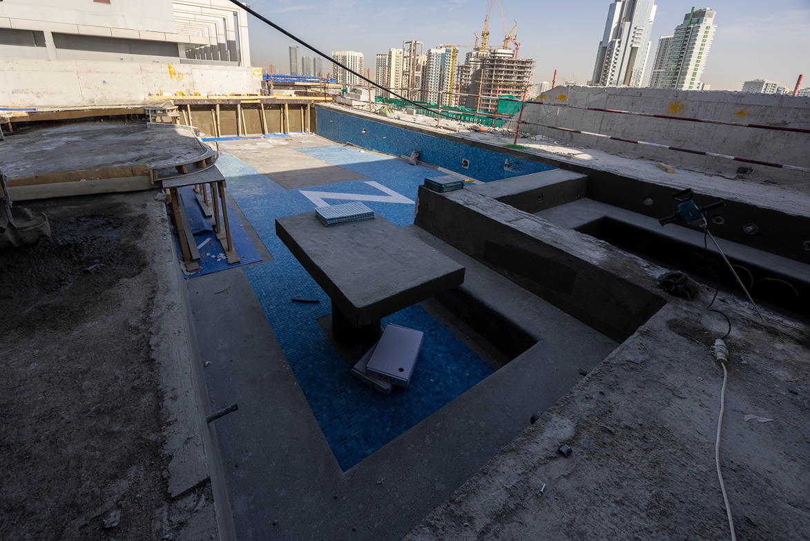 Pearl House By Imtiaz A partially constructed outdoor pool area with unfinished surfaces and construction materials, overlooking a city skyline.