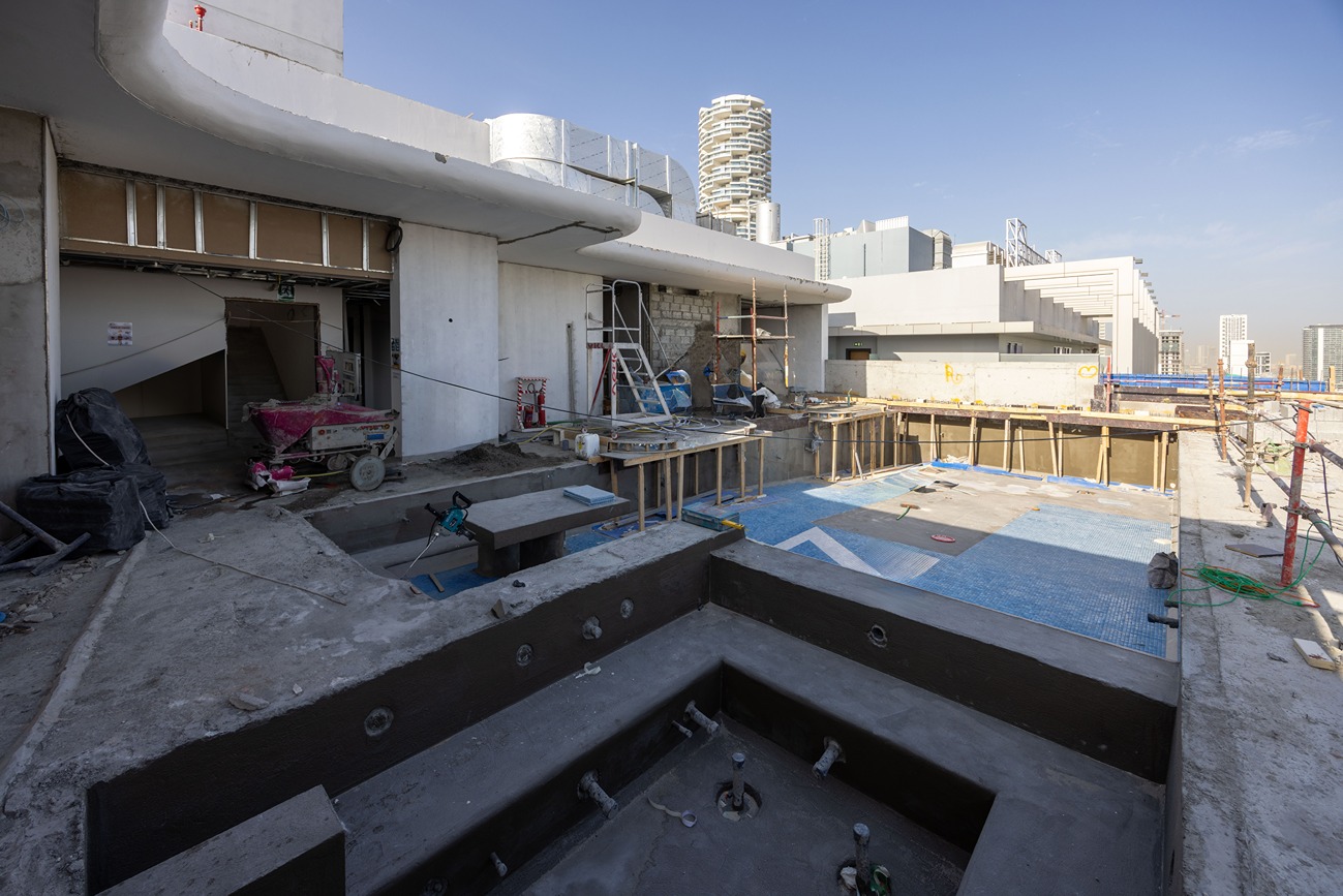 Pearl House By Imtiaz A construction site with an unfinished pool, scaffolding, and building materials under a clear blue sky.