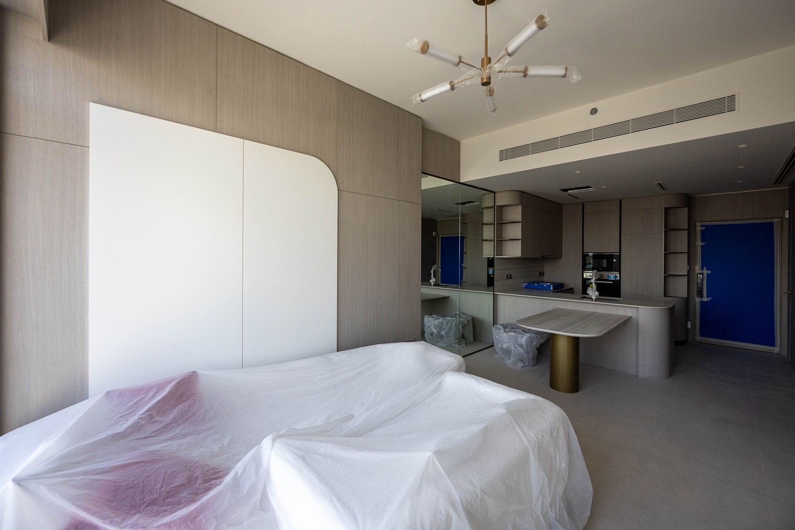 Pearl House By Imtiaz A modern, partially furnished room featuring covered furniture, minimalistic design, and a blue door.