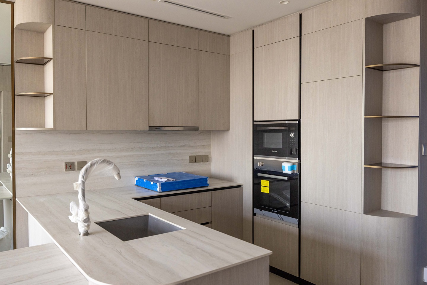 Pearl House By Imtiaz Modern kitchen featuring light wood cabinets, a sleek countertop, and built-in appliances including an oven and microwave.