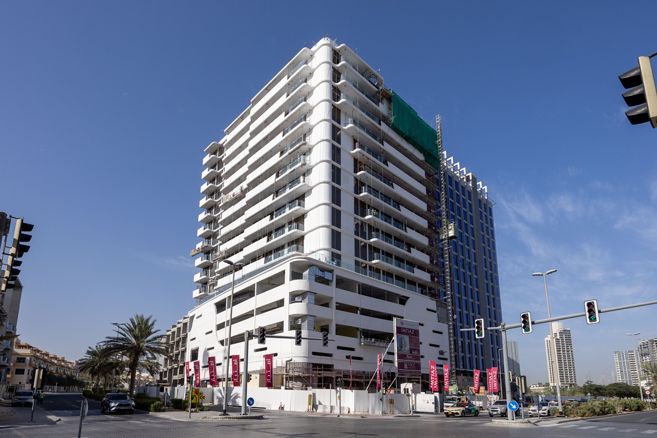 Pearl House By Imtiaz A modern multi-story building under construction, with traffic lights and palm trees nearby against a clear blue sky.