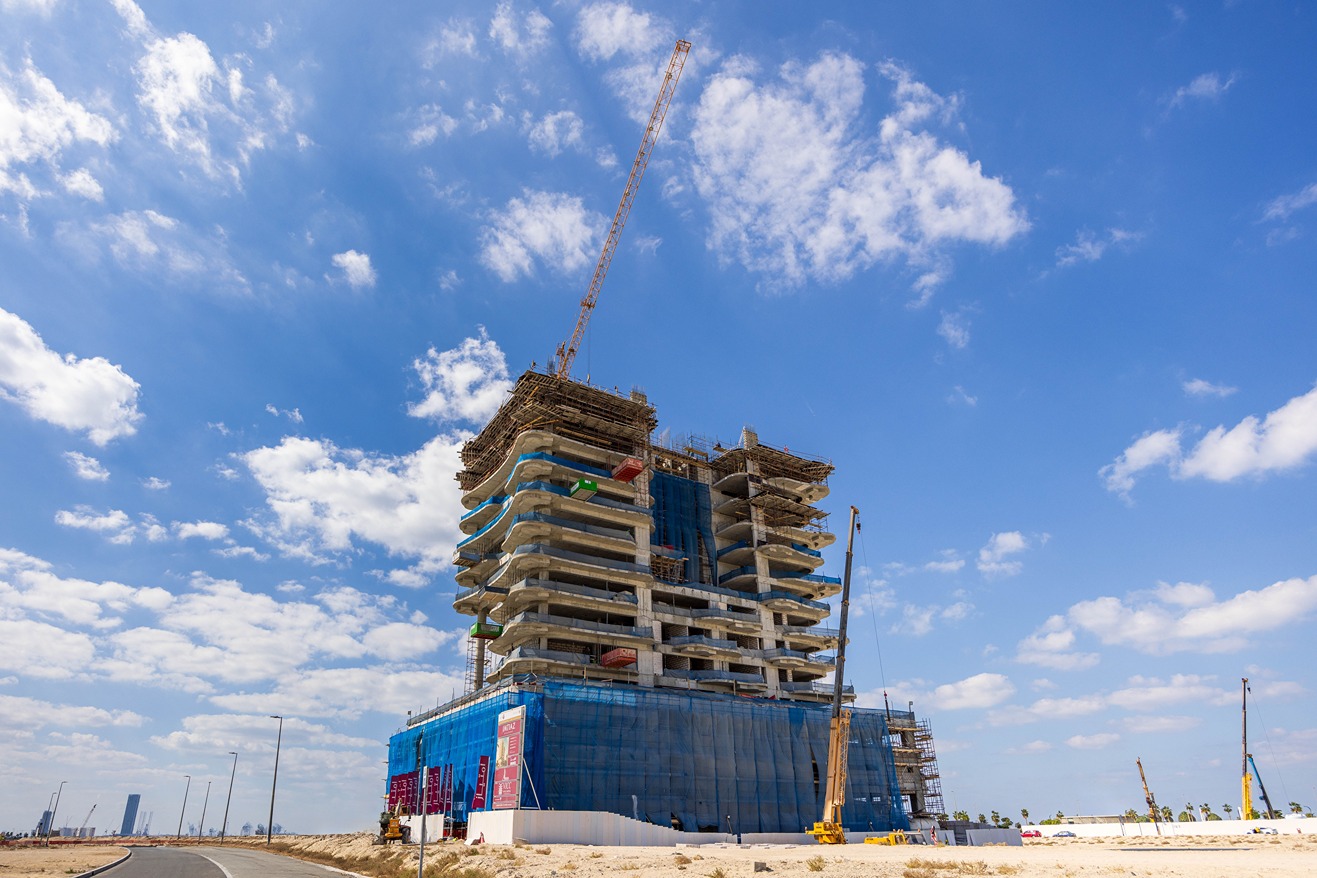 Beach Walk Residence Construction site of a multi-story building with cranes, scaffolding, and a blue sky filled with clouds.