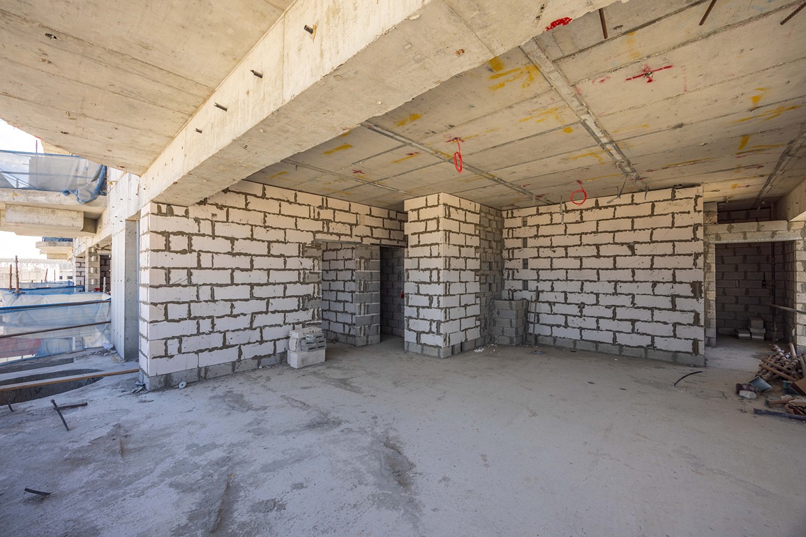 Beach Walk Residence An unfinished interior space with concrete walls, exposed beams, and construction materials scattered on the floor.