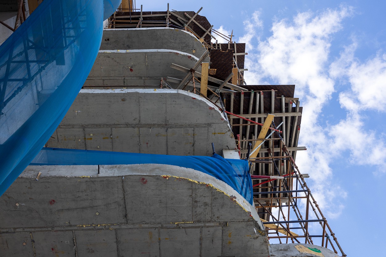 Beach Walk Residence Construction site with concrete structure, scaffolding, and blue fabric on a cloudy day.