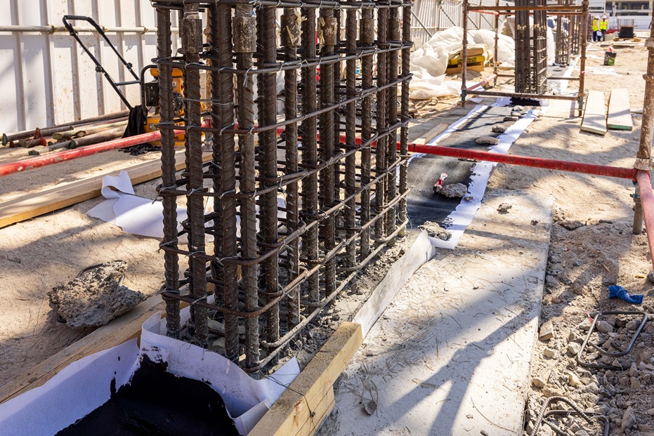 Beach Walk Iii By Imtiaz A construction site featuring metal rebar structures, concrete mixture, and wooden supports on a sandy surface.