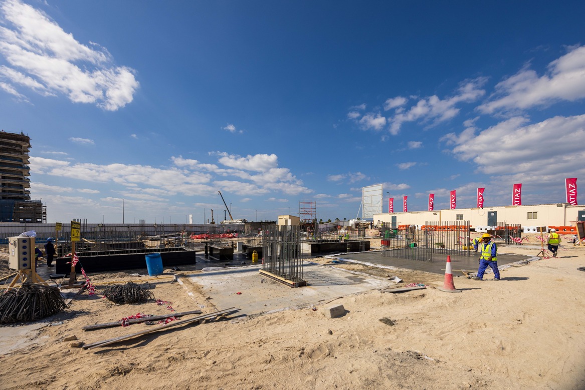 Beach Walk Iii By Imtiaz Construction site with workers, equipment, and building materials under a blue sky with clouds.