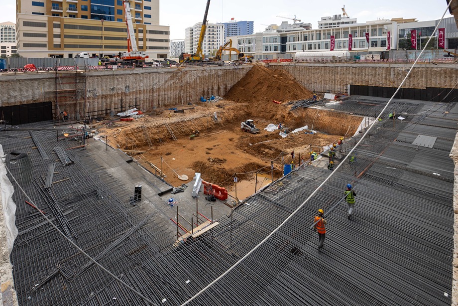 Cove Edition I By Imtiaz 1 Construction site with workers and machinery, a large excavation area, and piles of earth and rebar visible.