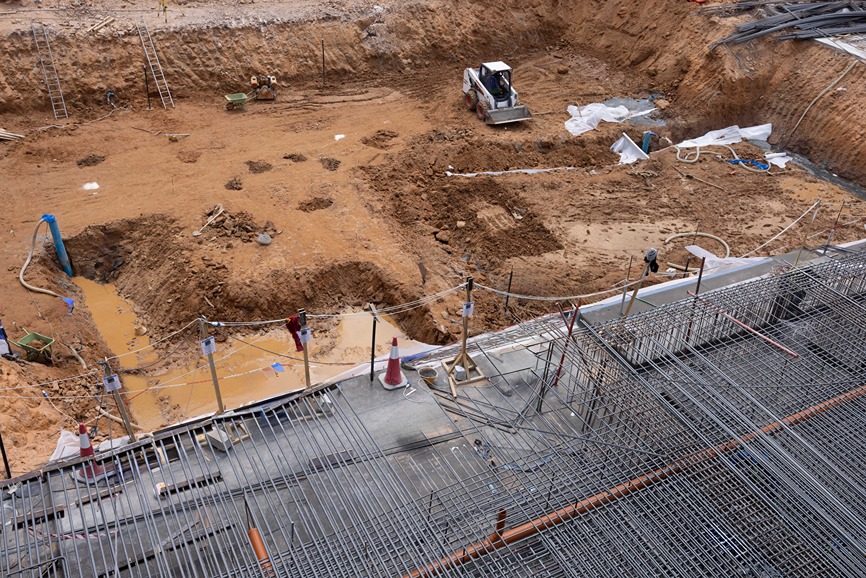 Cove Edition I By Imtiaz 1 Construction site with heavy machinery, excavated dirt, and scaffolding in a large, open trench area.