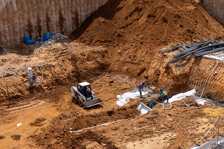 Cove Edition I By Imtiaz 1 Construction site with heavy machinery, workers, and piles of dirt and debris in an excavation area.