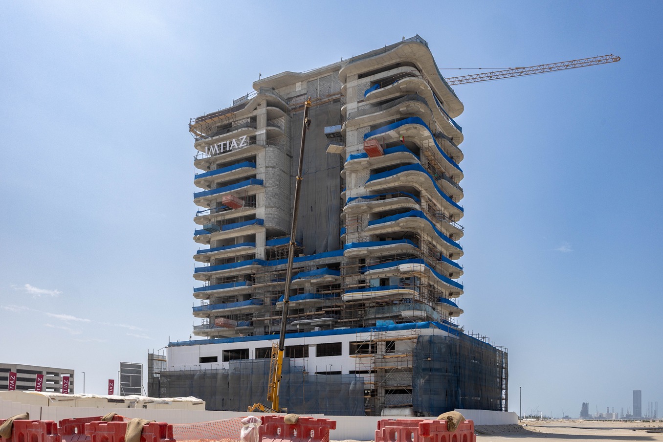 Beach Walk Residence A partially constructed high-rise building with scaffolding and a crane, under a clear blue sky.