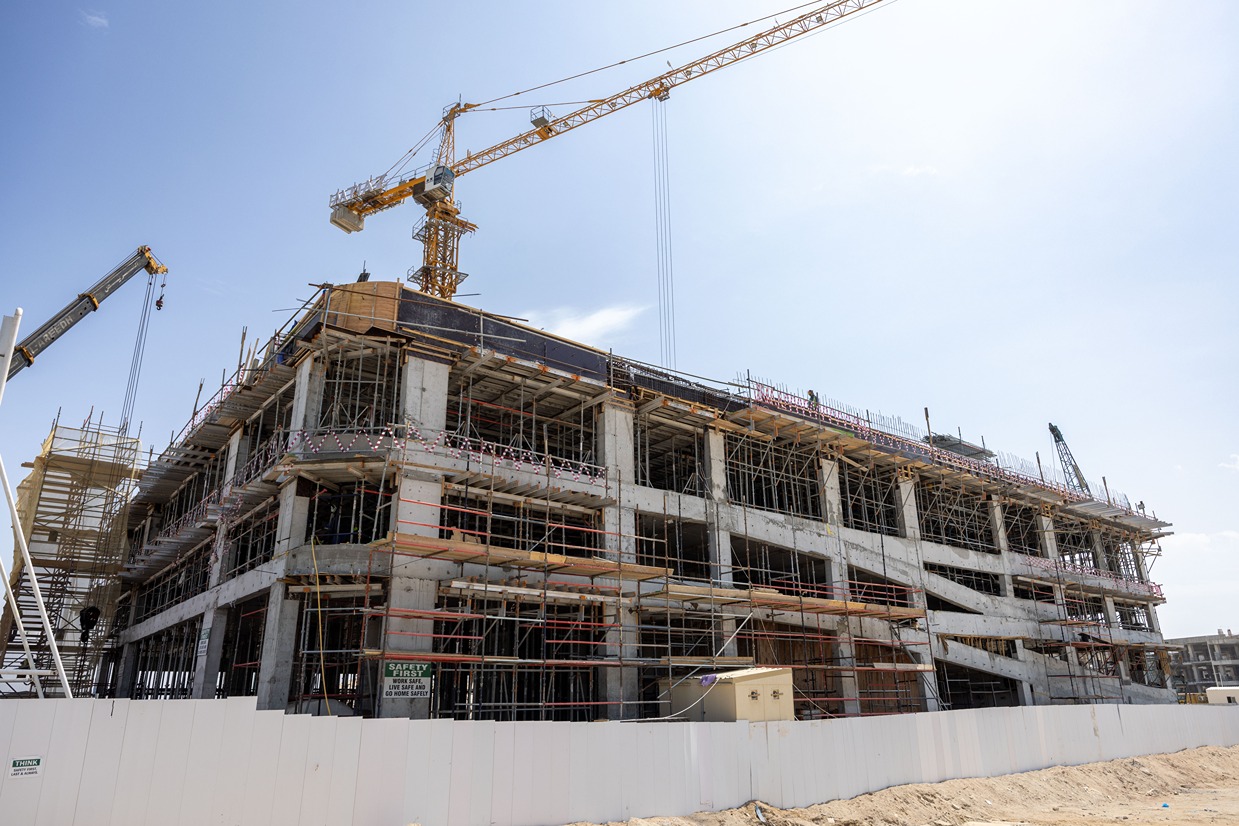 Beach Walk Iii By Imtiaz A large construction site featuring a partially built multi-story building with cranes and scaffolding against a blue sky.