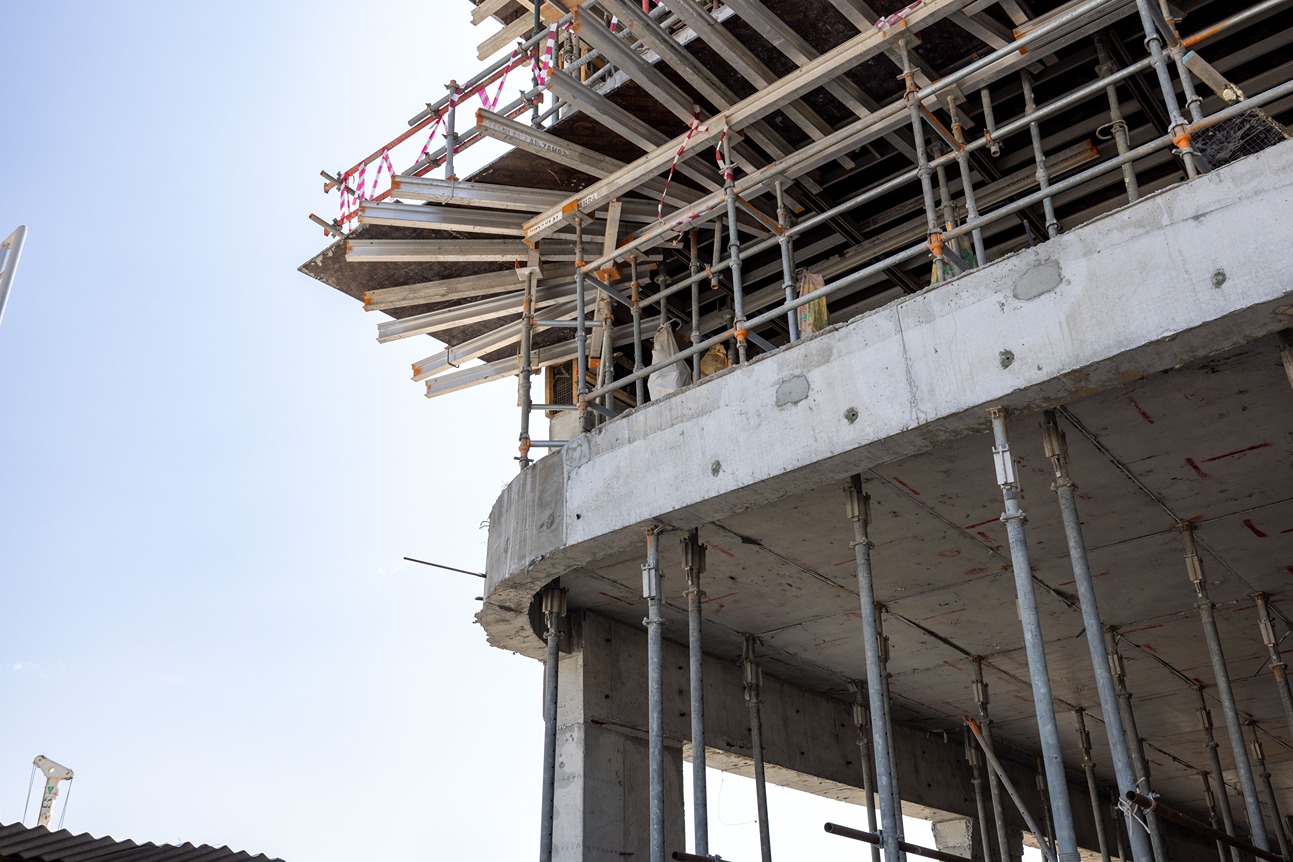 Beach Walk Iii By Imtiaz Construction site featuring scaffolding and support beams underneath a concrete building structure with clear sky.