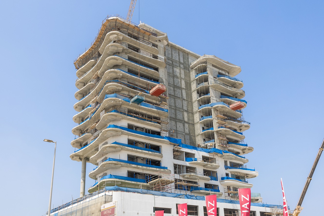 Beach Walk Residence A partially constructed high-rise building with curved balconies, scaffolding, and a clear blue sky background.