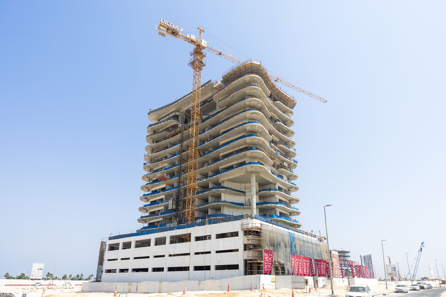 Beach Walk Residence A partially constructed building with a crane, featuring curved floors and scaffolding under a clear blue sky.