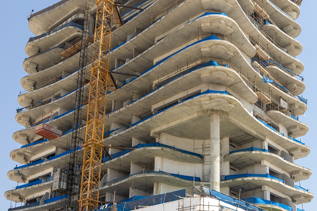 Beach Walk Residence A partially constructed building with multiple curved floors, scaffolding, and a yellow construction crane.