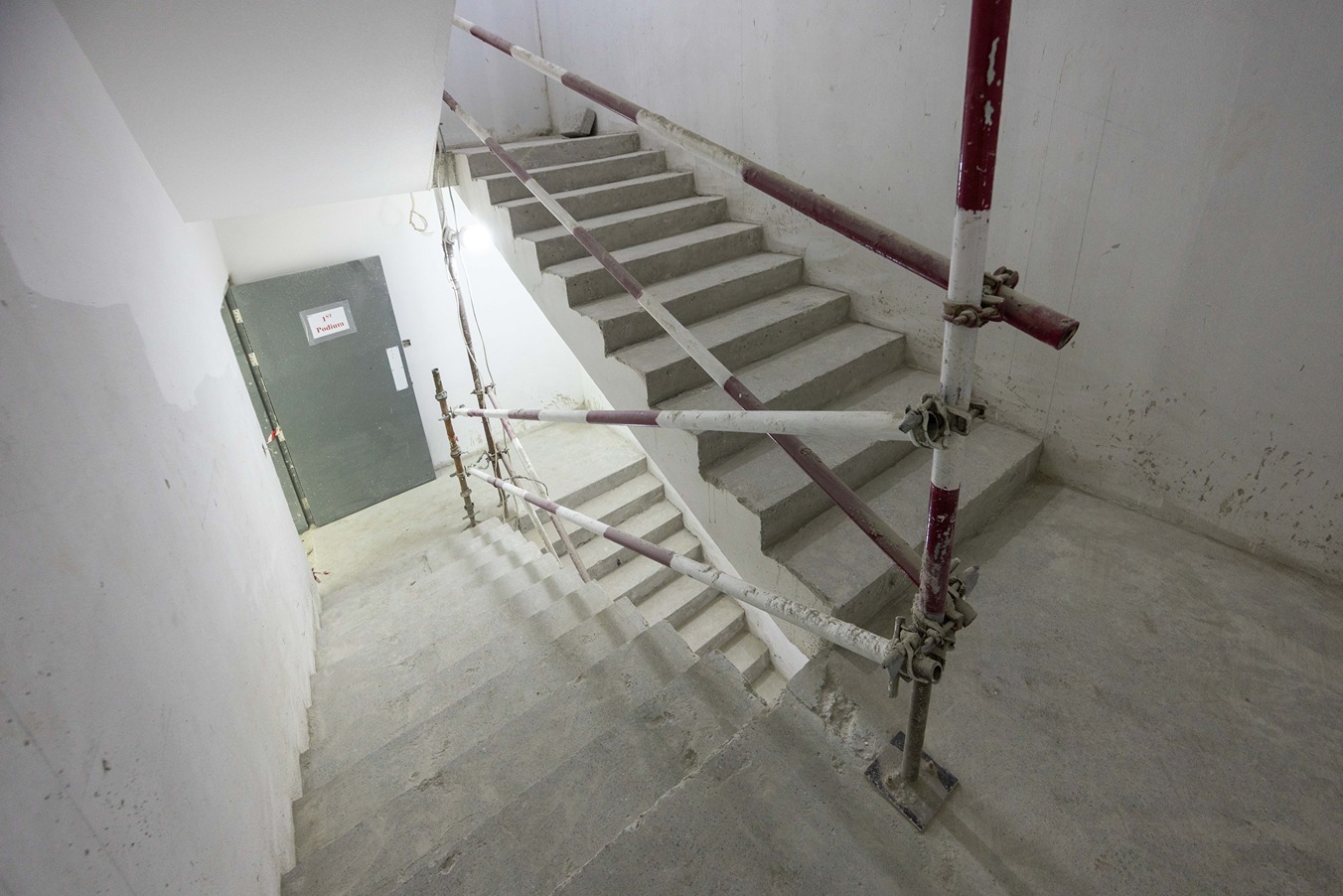 Beach Walk Residence A staircase with unfinished concrete steps, surrounded by scaffolding and leading to a gray door marked "1st Floor."