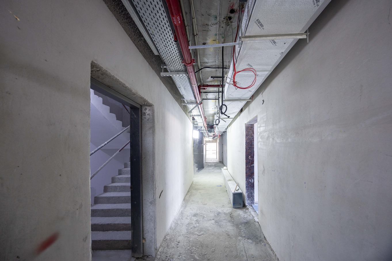 Beach Walk Residence A long, well-lit corridor with exposed walls, open doorways, and a staircase visible on the left side.