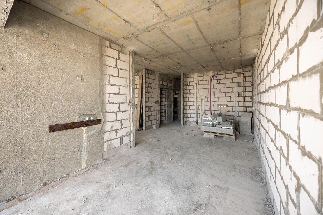 Beach Walk Residence An unfinished room with bare concrete walls, a dusty floor, and construction materials scattered around.