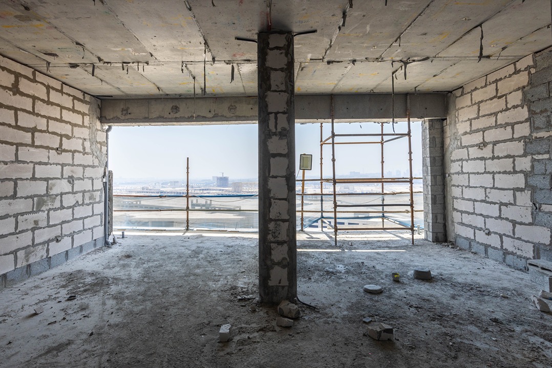 Beach Walk Residence An unfinished room with a concrete pillar, brick walls, and scaffolding, offering a view of the city skyline.