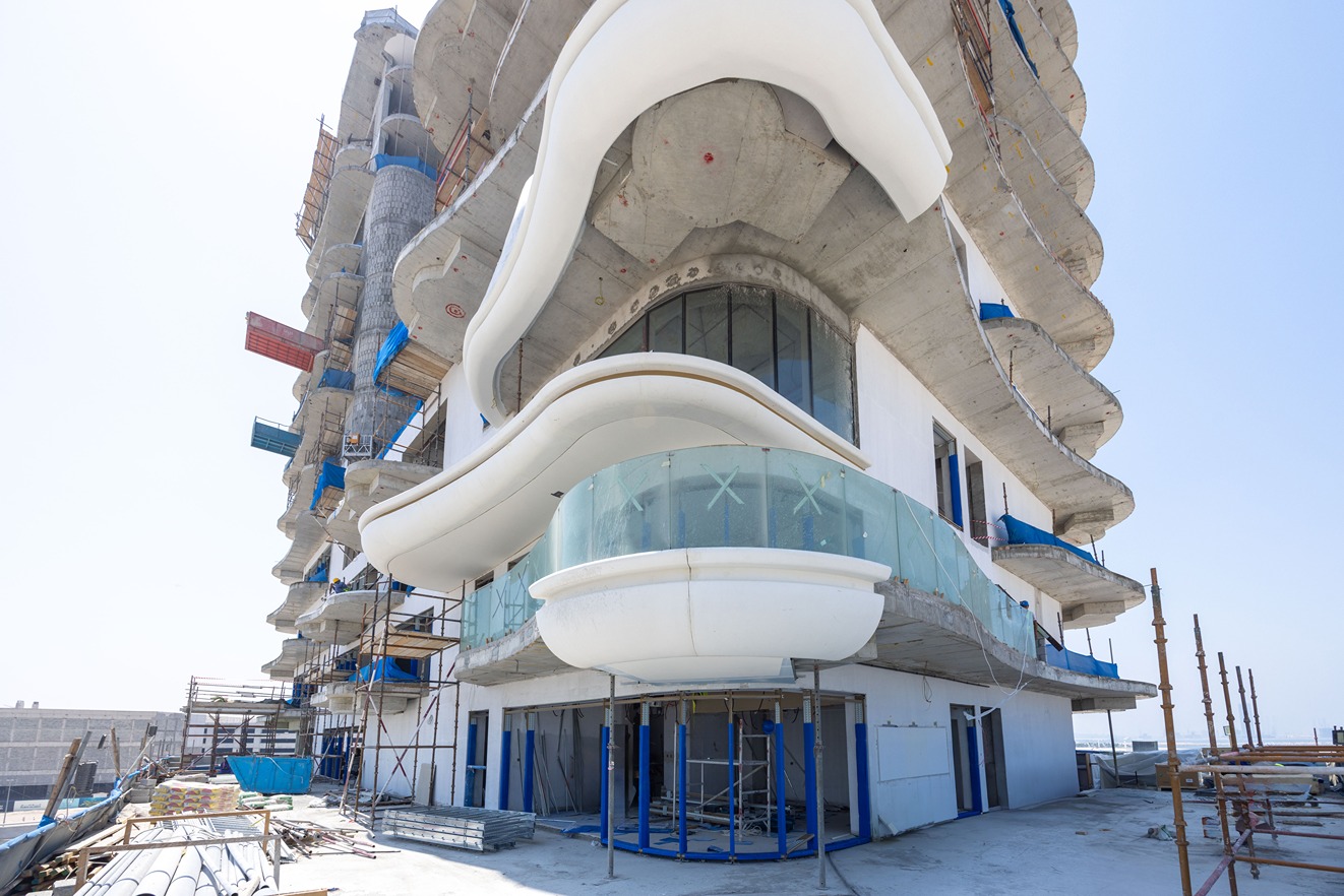 Beach Walk Residence A partially constructed building featuring curved balconies and scaffolding, with a clear blue sky in the background.