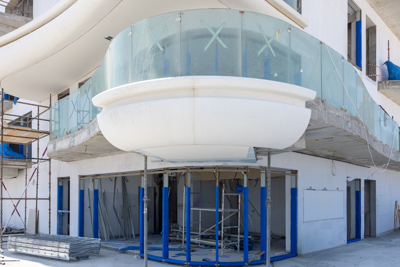 Beach Walk Residence A construction site featuring a modern building with a curved glass balcony and scaffolding in the foreground.