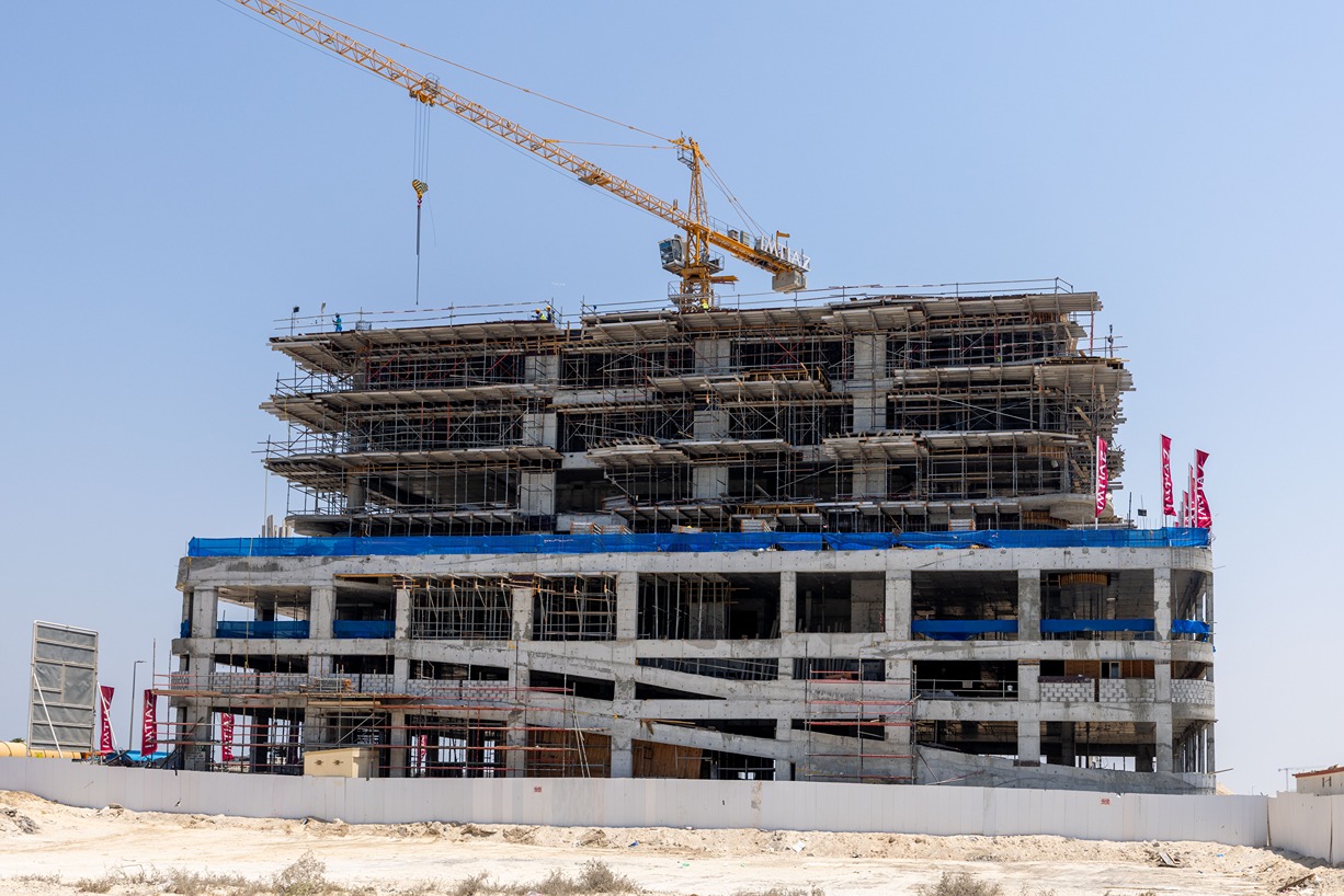 Beach Walk Iii By Imtiaz Half-finished building under construction with scaffolding and a crane against a clear blue sky.