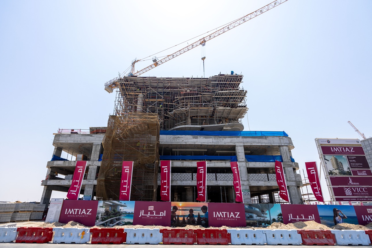 Beach Walk Iii By Imtiaz A construction site with a partially built structure, scaffolding, and construction signage in a clear sky.