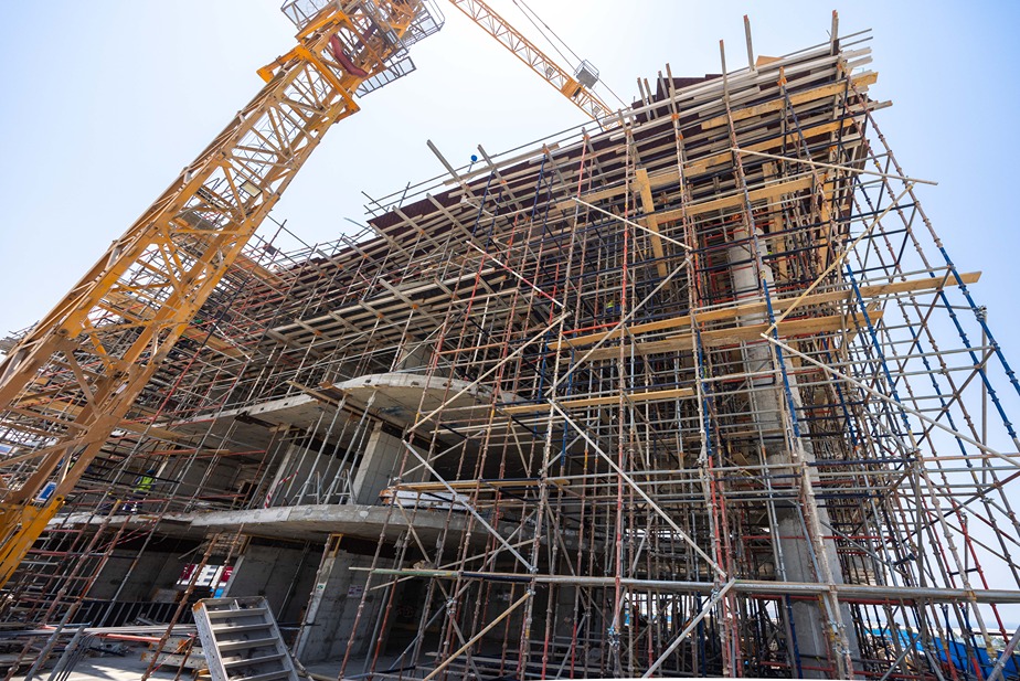 Beach Walk Iii By Imtiaz A construction site featuring a framework of scaffolding, a tower crane, and partially built concrete structure.