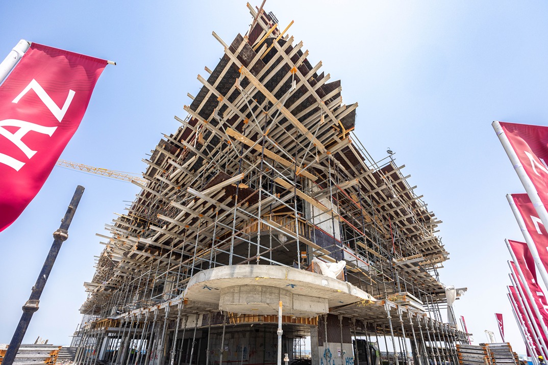 Beach Walk Iii By Imtiaz Construction site featuring a large building with scaffolding and cranes, against a clear blue sky.