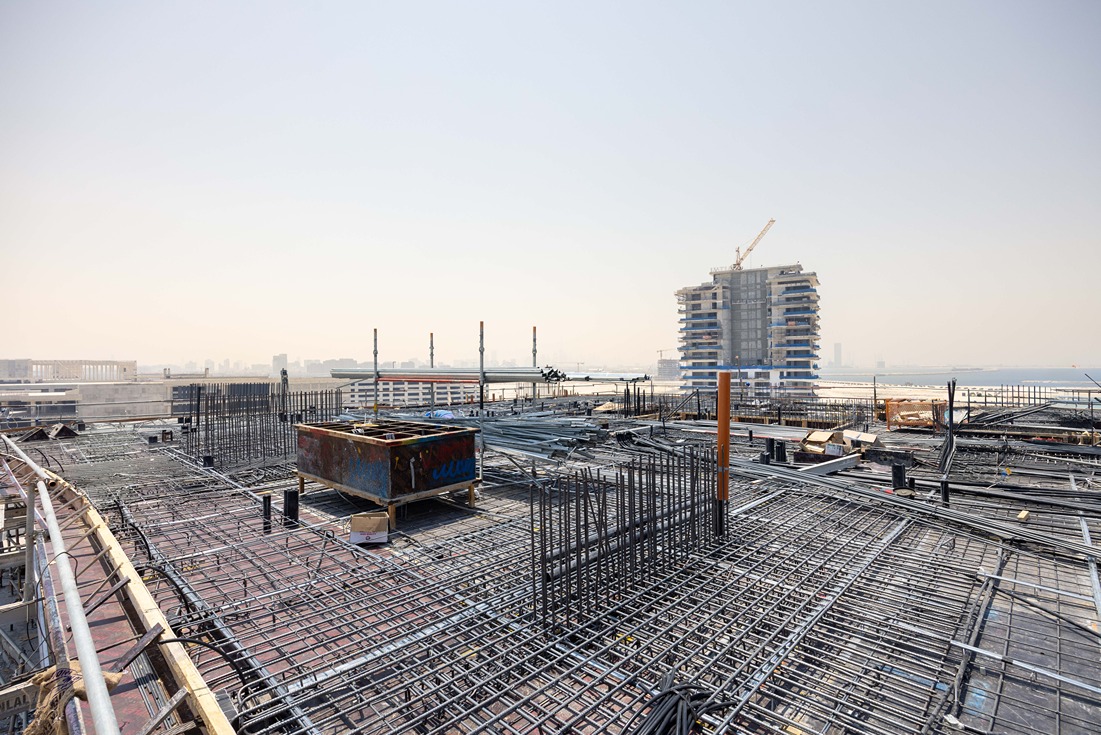 Beach Walk Iii By Imtiaz A construction site featuring a rebar framework and a partially finished building in the background.