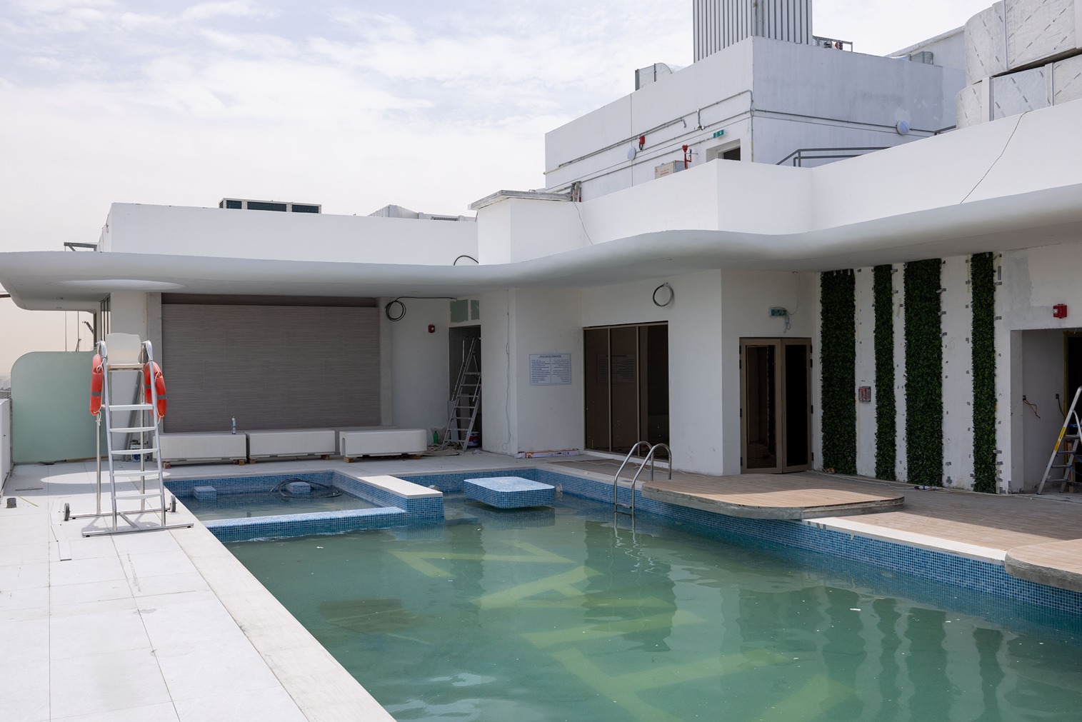 Pearl House By Imtiaz A rooftop pool area featuring a partially filled pool, lounge chairs, and a contemporary design against a cloudy sky.