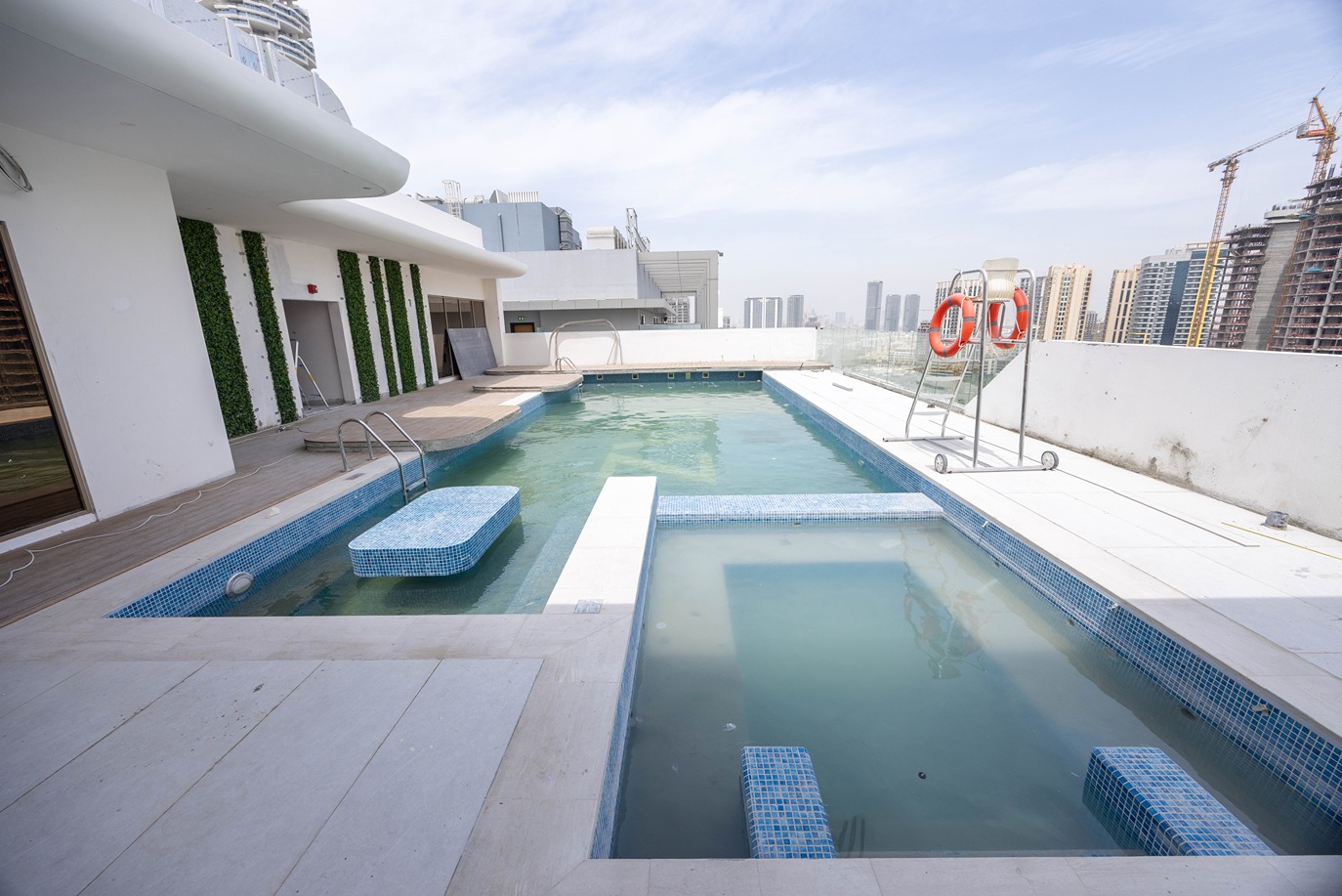 Pearl House By Imtiaz Rooftop pool area featuring two pools, lounge seating, and a lifeguard chair with city skyline in the background.