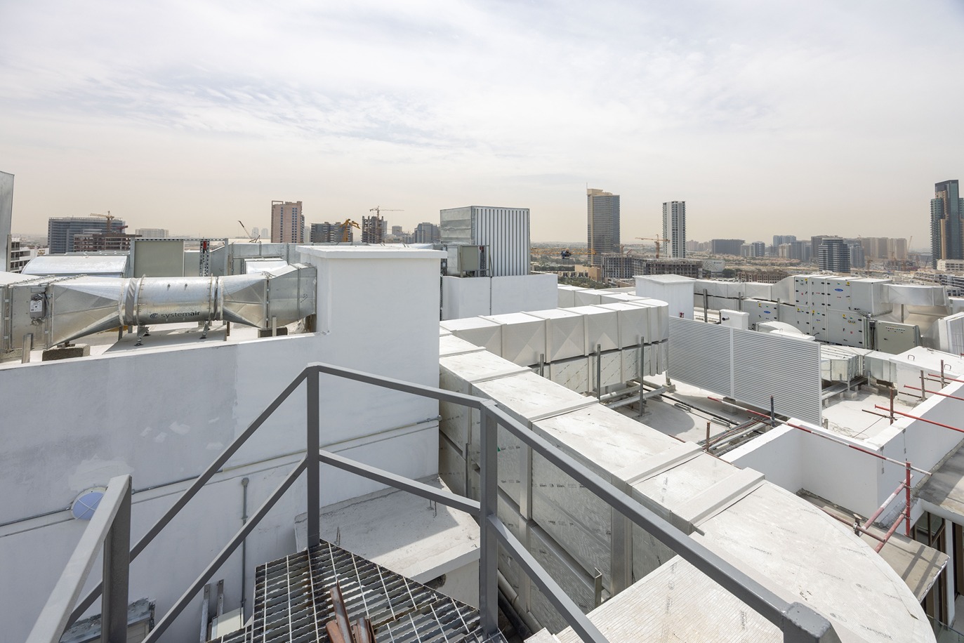 Pearl House By Imtiaz A rooftop view featuring HVAC systems with urban skyscrapers and construction sites in the background under a clear sky.