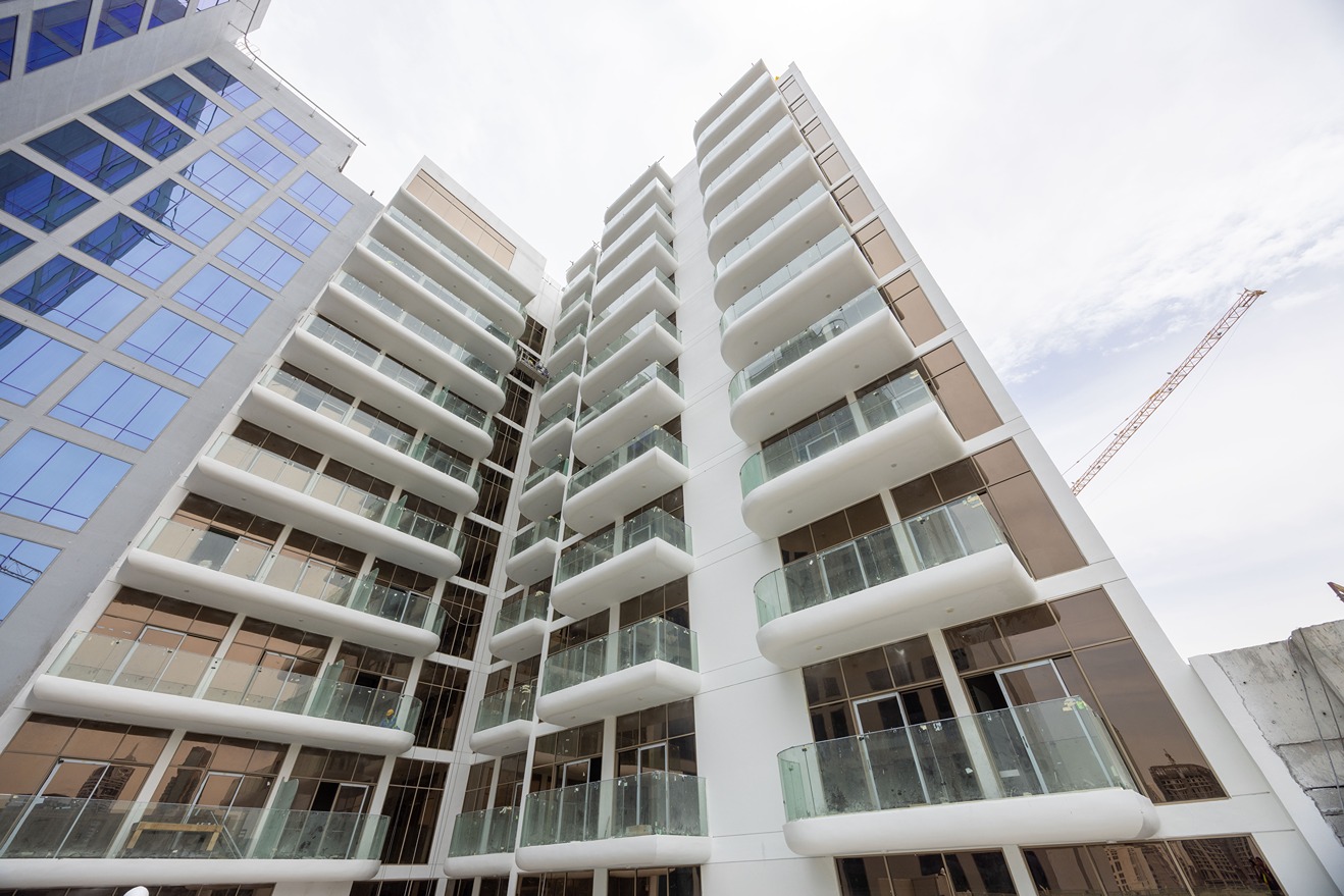 Pearl House By Imtiaz A modern building with several balconies, featuring large glass windows and a construction crane in the background.