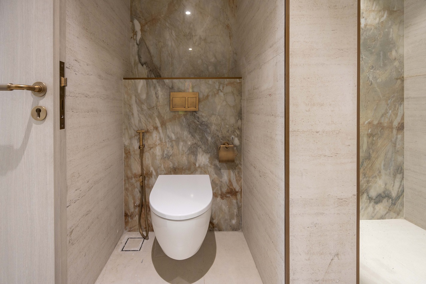 Pearl House By Imtiaz A modern bathroom featuring a sleek white toilet, marble walls, and elegant gold fixtures.