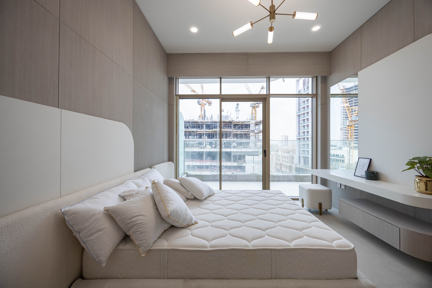 Pearl House By Imtiaz A modern bedroom featuring a plush bed with pillows and a large window showing a construction view outside.