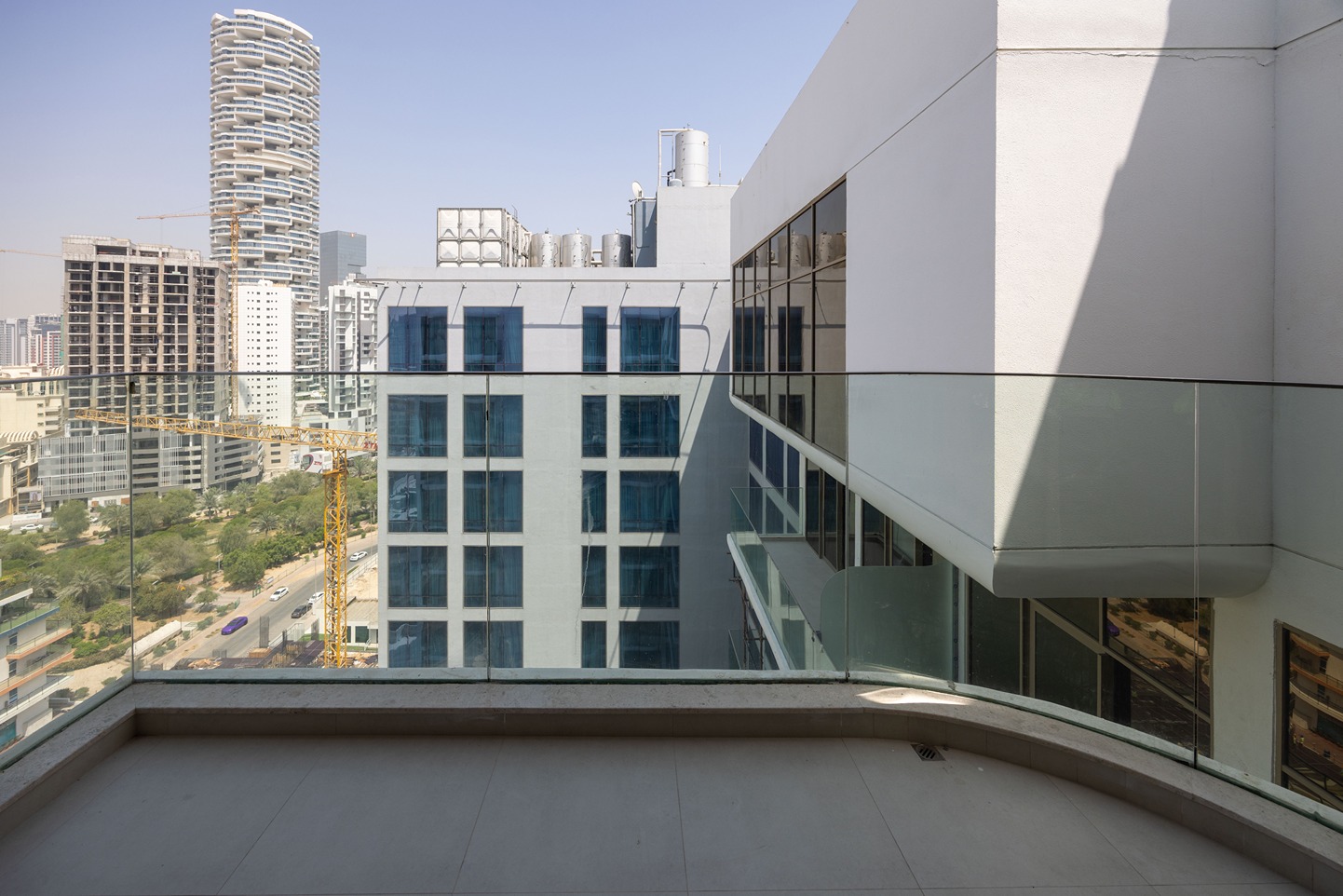 Pearl House By Imtiaz A modern balcony view showing glass railing, neighboring buildings, and a construction crane against a clear sky.