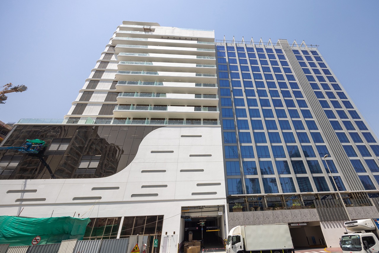 Pearl House By Imtiaz A tall, modern building with a glass facade and balcony features, showing construction elements in the foreground.