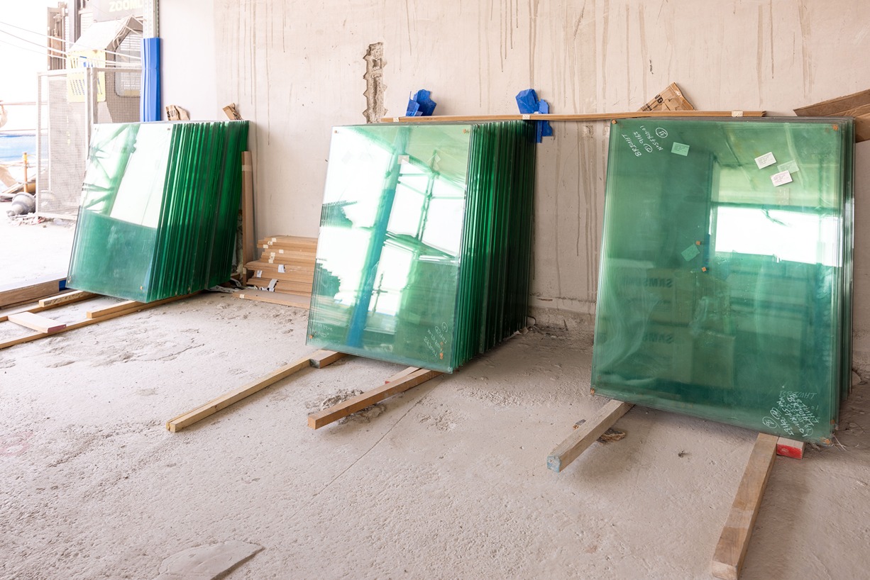 Beach Walk Residence Stacks of green-tinted glass panels are leaning against a wall inside a construction site.